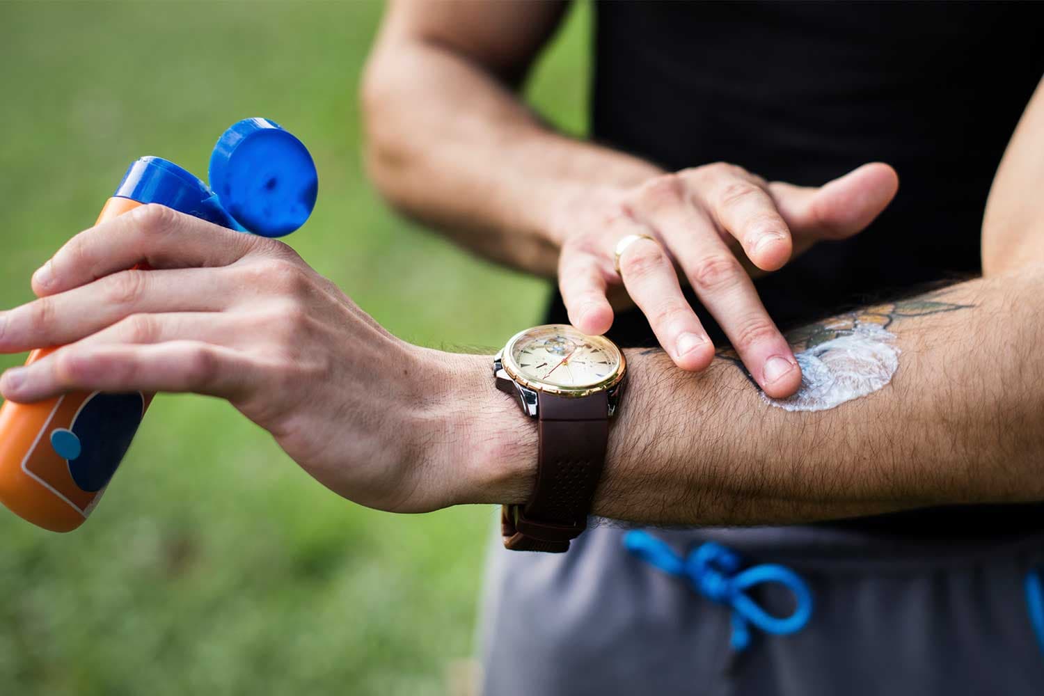 A man wearing exercise clothing rubs sunscreen into his forearm.