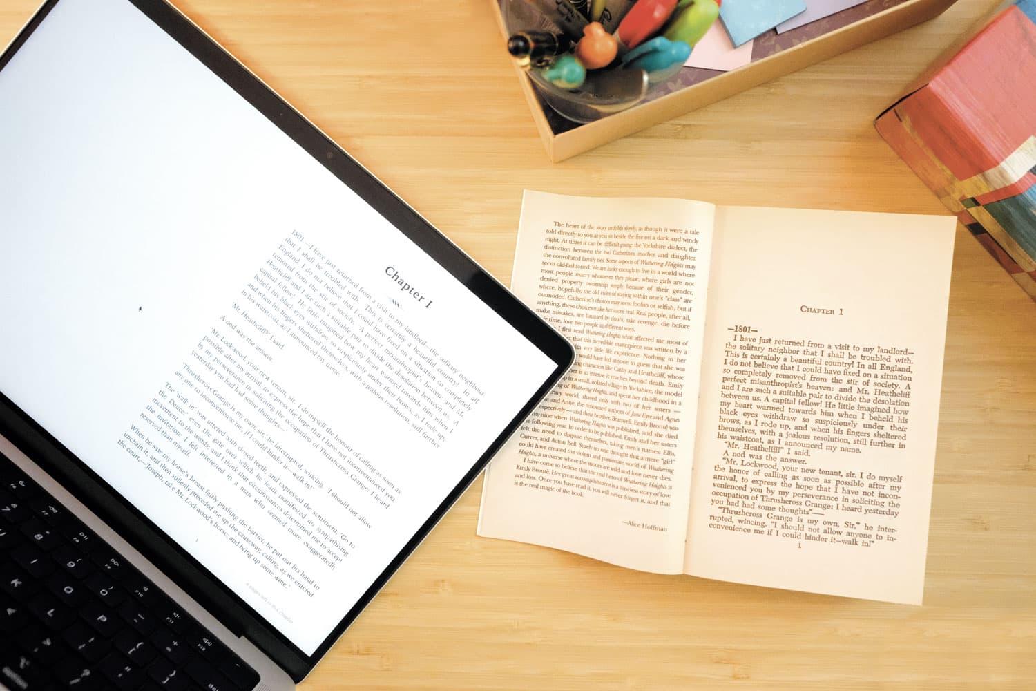 On a wooden desk, a laptop displays an e-book of Emily Brontë’s Wuthering Heights, next to a print version of the book.