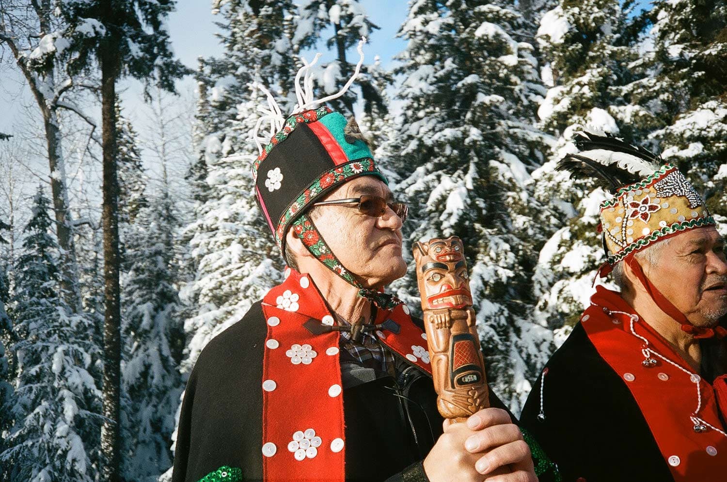 Chief Namoks of the Wet'suwet'en in traditional clothing standing in front of large snow-covered trees.