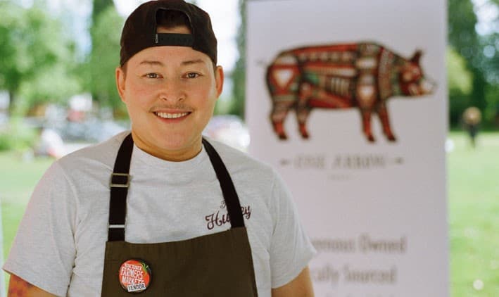 Headshot of Heat Laliberte. He has light skin and wears a black cap backwards, a grey t-shirt and black apron.