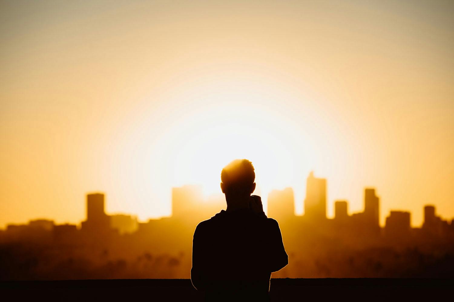 A silhouette of a man with a skyline of the city in the background at sunset.